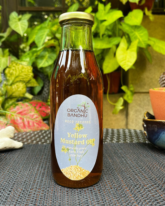 Bottle of Organic Bandhu Yellow Mustard Oil on a textured surface with plants in the background