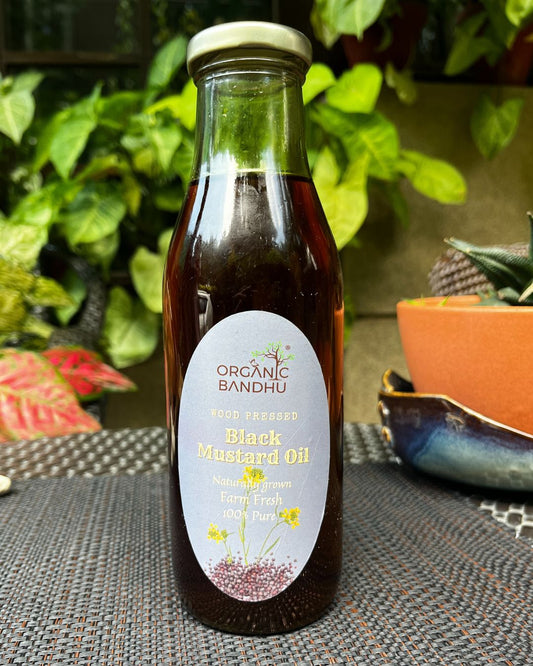 Bottle of Organic Bandhu Black Mustard Oil on a textured surface with plants in the background